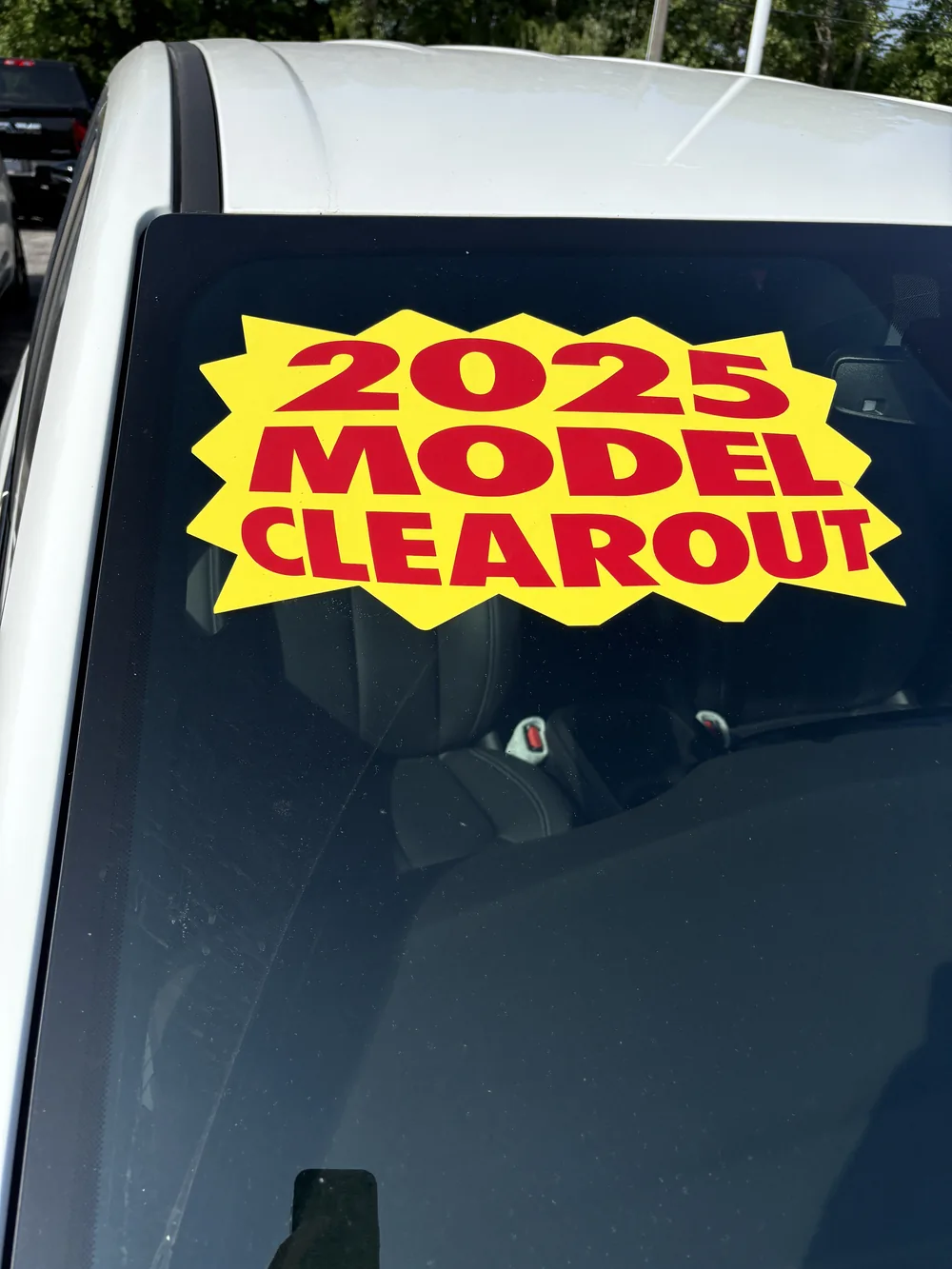 Red and yellow 2025 Model Clearout promotional decal on a vehicle windshield